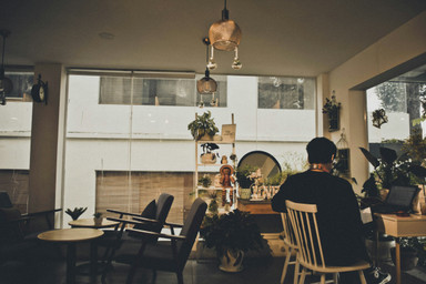A modern apartment living room where a man sits, facing away from us, watching his computer screen