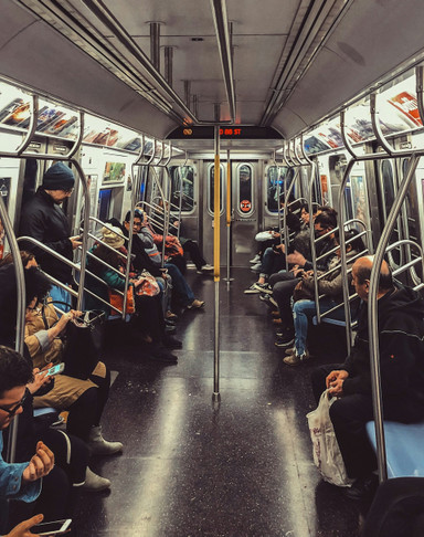 Looking down the center a New York subway car, where an array of people sit talking and reading their phones