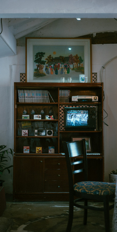 A tall and narrow wooden tv cabinet against the wall, with a tape player and music and vhs tapes.