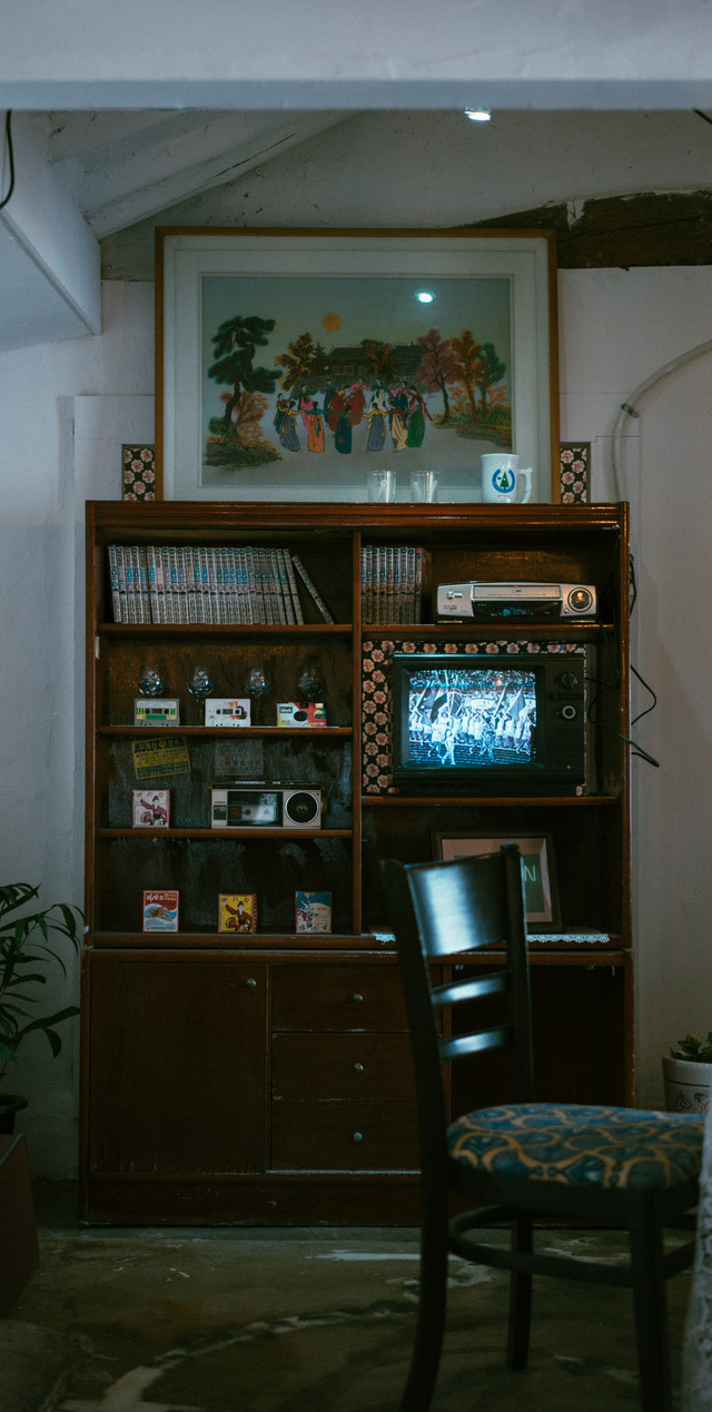A tall and narrow wooden tv cabinet against the wall, with a tape player and music and vhs tapes.