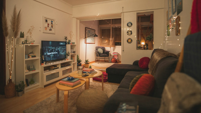 Evening in a cozy living room with nicknacs and lamps, with plush couches and chairs around a lit up television