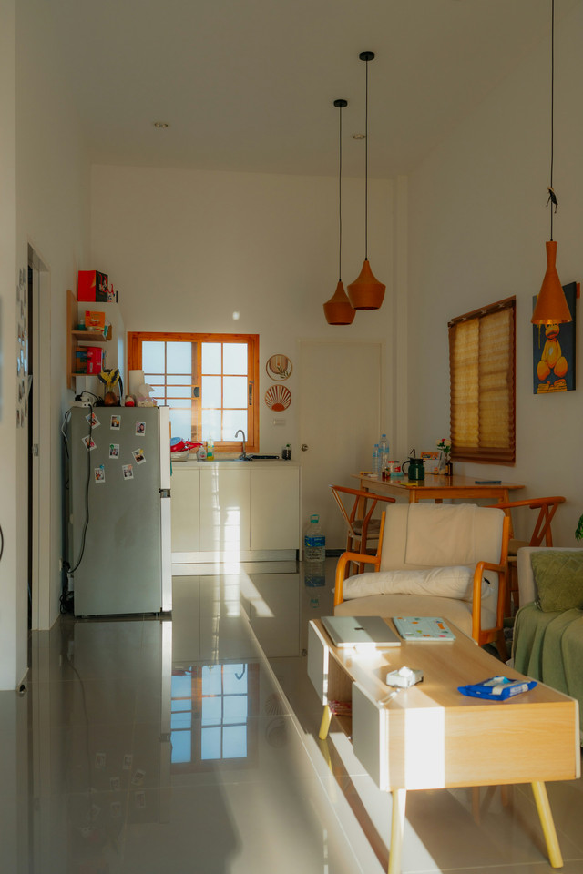 A modern small apartment kitchen with bright white tile floors and hanging orange lamps